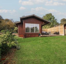 A cabin with a deck and grass area at Woodlands View in Leek