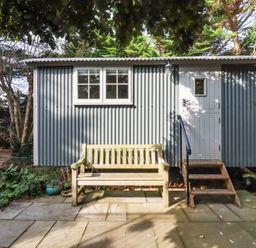 A shepherd hut with a wooden bench and plants at Hillbre Shepherd Hut in Padstow