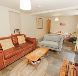 A living room with a sofa, coffee table, and dining area at Rock Cottage in Milnthorpe
