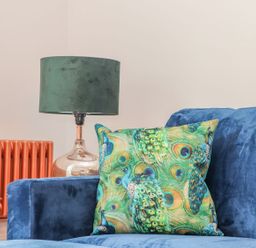 A living room featuring a blue sofa with a patterned pillow and a green lamp at Mews Retreat in Camborne