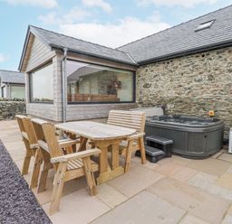 An outdoor area with a hot tub and wooden furniture at 2 Trem Y Mor Llanfwrog near Llanfachraeth