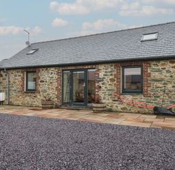 An outdoor view of a stone building with a patio at 2 Trem Y Mor Llanfwrog near Llanfachraeth