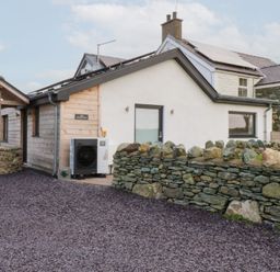 An exterior view of a house with a stone wall and driveway at Hen Penmynydd in Llanfwrog near Llanfachraeth