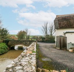 An outdoor scene with a bridge over water next to a house at Long Barn in Burton Bradstock