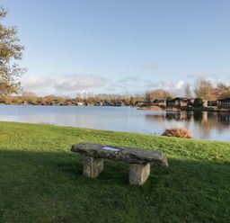 A lake with a stone bench and trees at Bluebell Lodge in Warton