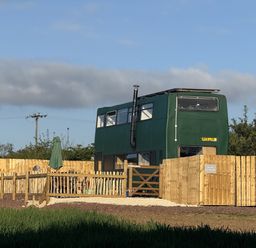 A green bus with a fence and outdoor seating at The Bus on the Hill, Huntsham near Bampton, Devon