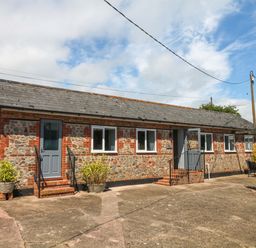 An outdoor view of a stone building with a blue door and windows at The Milk Shed in Plymtree