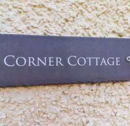 A slate sign displaying 'Corner Cottage' on an outdoor wall