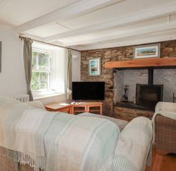 A living room with a fireplace and television at Blowing House Cottage near Perranporth