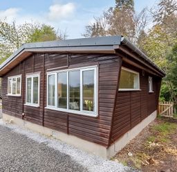 A wooden house with multiple windows and a gravel driveway