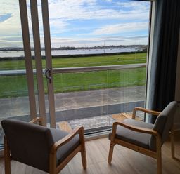 A living room with two chairs and a view of grass and water at Sea Fern House - 36 Poole