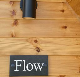 A wooden wall with a light fixture and a sign labeled Flow at Kirkapol Beach Pod - Flow Isle of Tiree