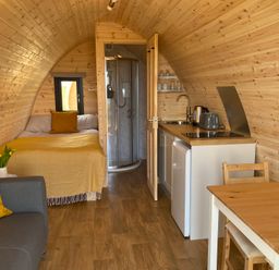A sleeping area with a sofa and kitchenette at Kirkapol Beach Pod - Flow Isle of Tiree