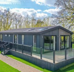 A lodge with a deck and glass railing at Isca Lodge - With Decking - Lodge 1 Wombleton