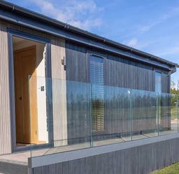 An exterior view of a lodge with glass railing and door at Isca Lodge - With Decking - Lodge 1 in Wombleton