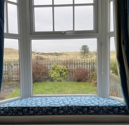 A window with a cushion overlooking a garden at Braeburn in Bamburgh