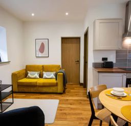 A living room with a yellow couch and dining table at Oakwood Apartment in Llanrwst