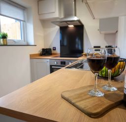 A kitchen with wine glasses and a bottle on a wooden surface at Ash Cottages in Llanrwst