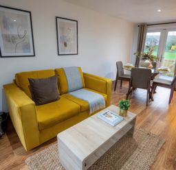 A living room with a yellow sofa and dining area at Fir Cottages in Llanrwst