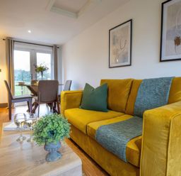 A living room with a yellow sofa and dining area at Silver Birch Cottage in Llanrwst