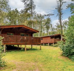 A log cabin with a deck surrounded by trees at Cedar Lodge in Louth
