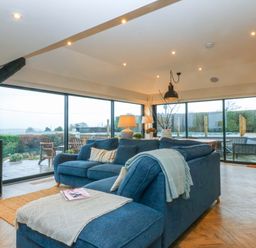 A living room with a wood stove and large windows at Bryn Mor Cottage in Mynytho near Llanbedrog