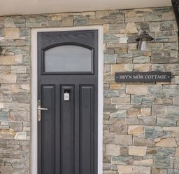 The entrance door with a stone wall and a sign at Bryn Môr Cottage in Mynytho near Llanbedrog