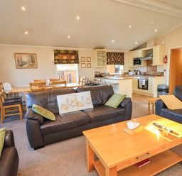 A living room with a sofa, coffee table, and dining area at Kingfisher Lodge