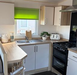 A kitchen with cabinets, sink, stove, and appliances at The Beachside Hideout - St Michaels Caravan Park, Towyn