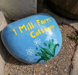 A painted stone with the text 1 Mill Farm Cottages and flowers at 1 Mill Farm Cottages Narberth