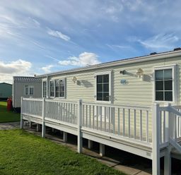 A mobile home with a deck and grassy area at Gainc Bach in Abergele