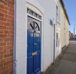 A blue front door next to a brick wall at Rope Cottage in Bridport