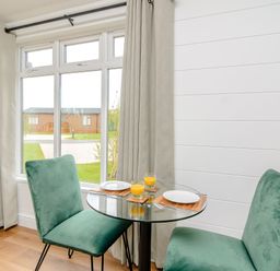 A dining room with a glass table and green chairs at The Castor in Kings Cliffe