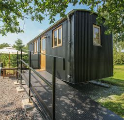A shepherd's hut with steps and a table under an umbrella at Dave’s Place Broadstone near Munslow