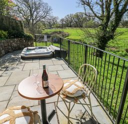 An outdoor patio with a hot tub and a table with a wine bottle and glasses at Rose Apartment in Old Walls, Llanrhidian, Gower