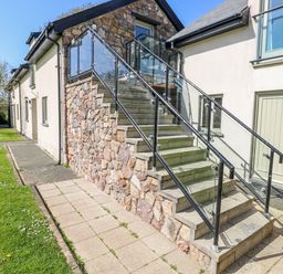 Stairs with glass railing leading to a door at Willow Apartment in Oldwalls, Llanrhidian, Gower
