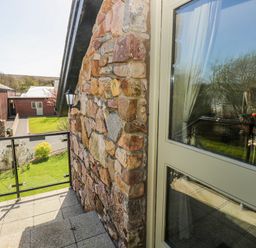 An outdoor area with a stone wall and glass railing at Willow Apartment in Oldwalls, Llanrhidian, Gower