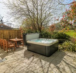 A garden with a hot tub and wooden furniture at Ivy Cottage Oldwalls, Llanrhidian, Gower