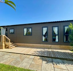 An exterior view of a cabin with a wooden deck at Acacia Waterside Spa Carlton Miniott near Thirsk