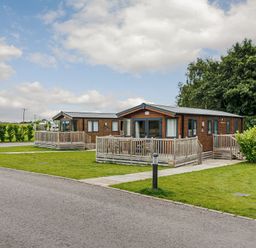 Two wooden chalets with decking in an outdoor area at Alder Spa in Carlton Miniott near Thirsk