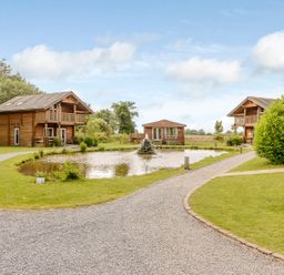 An outdoor area with lodges and a pond at Banyan Waterside Spa Carlton Miniott near Thirsk