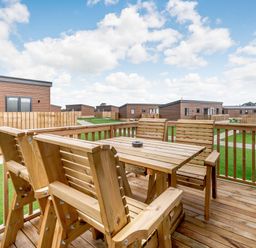 A patio area with a wooden table and chairs at Kinder Spa (Pet) Carlton Miniott near Thirsk