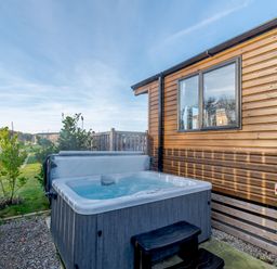 An outdoor area with a hot tub beside a wooden cabin at Alder Spa (Pet) Carlton Miniott near Thirsk