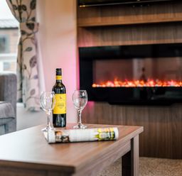 A living room with a wine bottle and glasses on a coffee table at Larch Waterside Spa Carlton Miniott near Thirsk