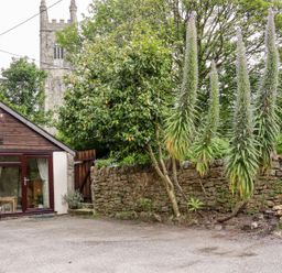 An exterior view of a building with plants and a stone wall at Lannlyvri Lodge in Lanlivery near Lostwithiel