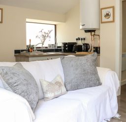 A living room with a sofa and kitchen area at Lannlyvri Lodge Lanlivery near Lostwithiel