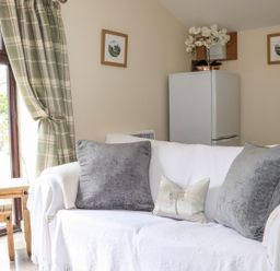 A living room featuring a sofa and a fridge at Lannlyvri Lodge in Lanlivery near Lostwithiel