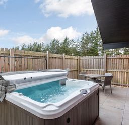 An outdoor patio with a hot tub and a table with chairs at Raeburn Premier Spa in Dundee