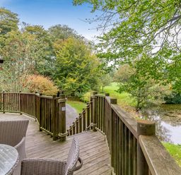 An outdoor area with a wooden deck overlooking trees and a pond at The Treehouse in Praze-An-Beeble