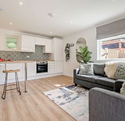 A kitchen area with white cabinets and bar stools at Klys 1.0 Spa Perranporth